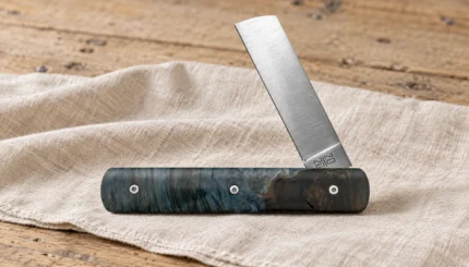Couteau 20/20 en marronnier stabilisé bleu entrouvert, posé sur un linge de lin sur un établi en bois.